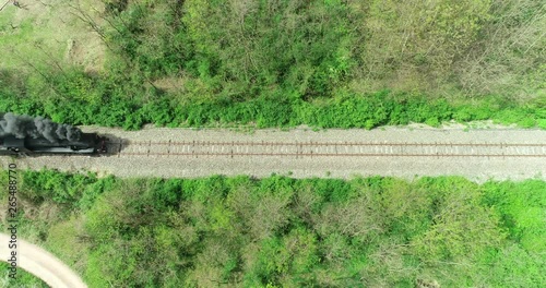 Historic train with steam locomotive and old carriages runs on the tracks in the countryside. Aerial view.