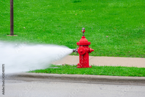 Red fire hydrant being flushed, high pressure water spraying forcefully