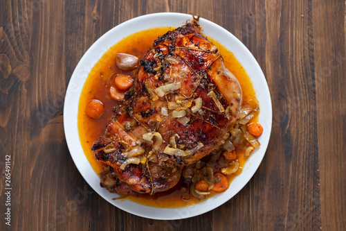 baked turkey leg with vegetables and herbs on white dish