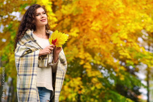 Young woman walks through the autumn park and gathers yellow red green leaves wrapped in a blanket