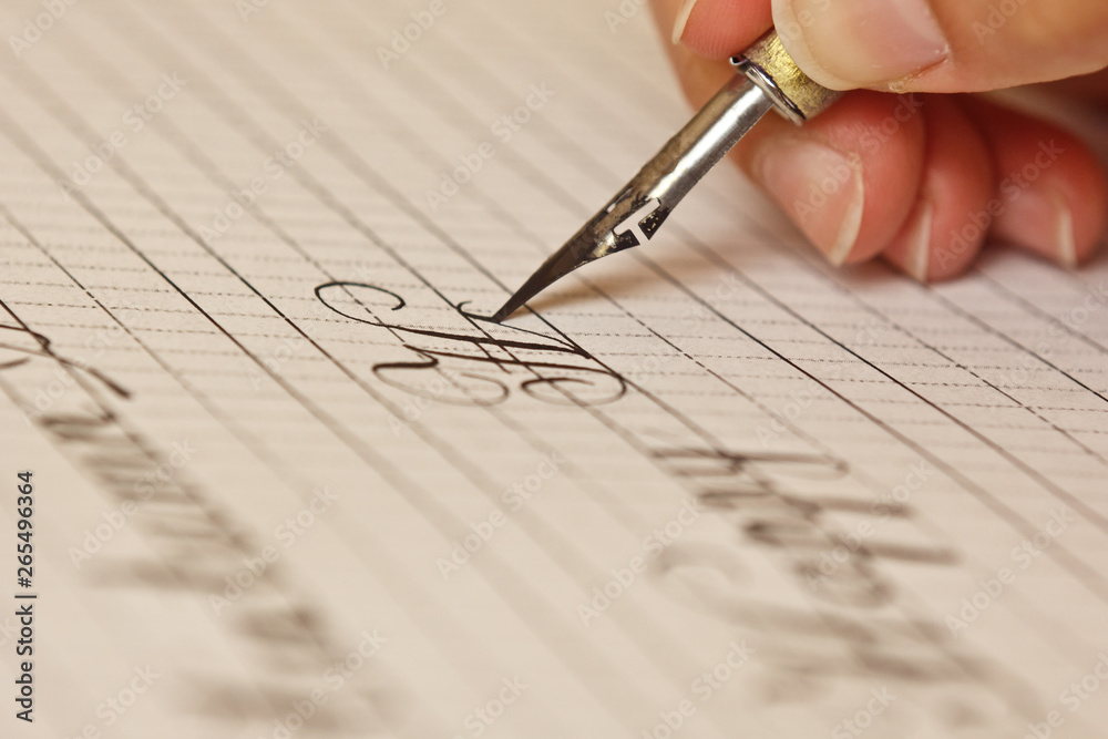 female hand writes with the inky pen on a white paper sheet with stripes. stationery on desk close up top view. spelling lessons and caligraphy exercises. Template, layout, background. macro female hand writes with the inky pen on a white paper sheet with stripes. stationery on desk close up top view. spelling lessons and caligraphy exercises. Template, layout, background. macro