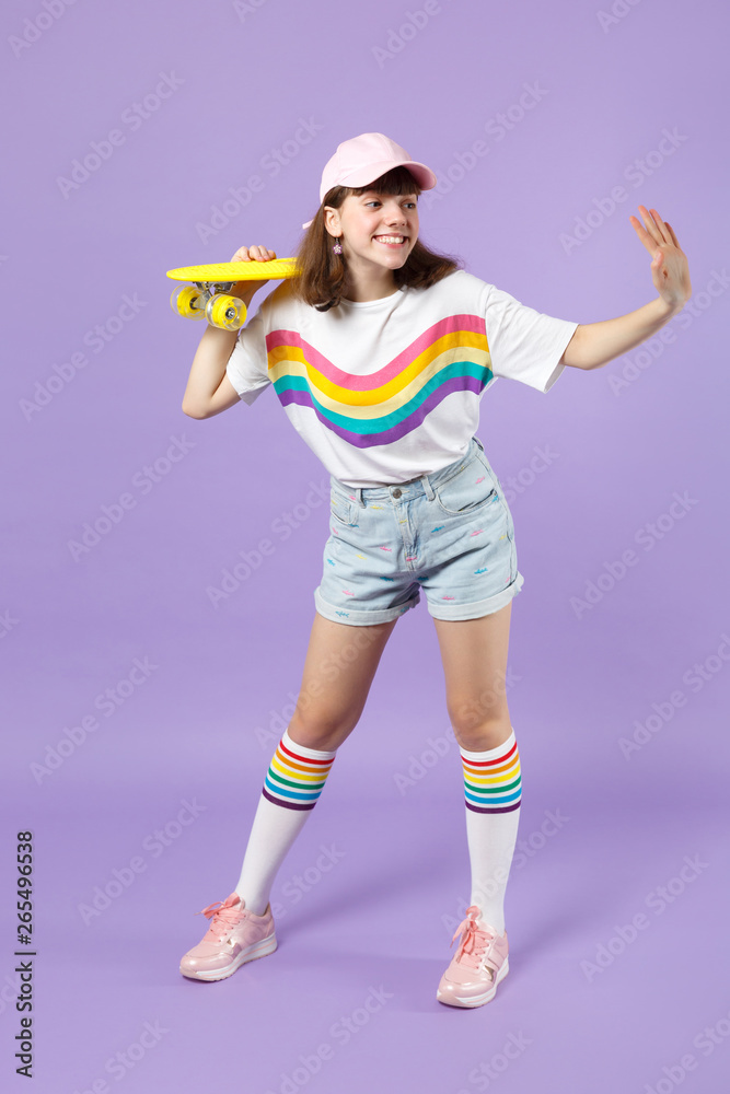 Pleasant teen girl hold skateboard looking aside, waving and greeting with hand as notices someone isolated on violet pastel background. People sincere emotions, lifestyle concept. Mock up copy space.