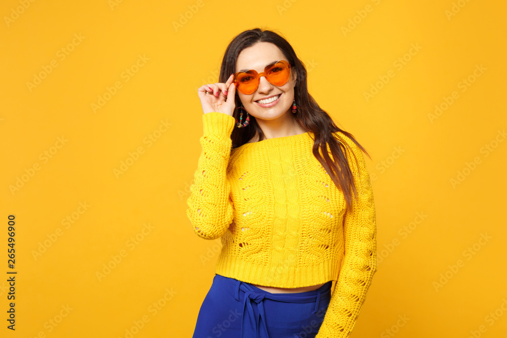 Portrait of smiling young woman in sweater, blue trousers, heart glasses standing, looking camera isolated on yellow orange background. People sincere emotions, lifestyle concept. Mock up copy space. Portrait of smiling young woman in sweater, blue trousers, heart glasses standing, looking camera isolated on yellow orange background. People sincere emotions, lifestyle concept. Mock up copy space.