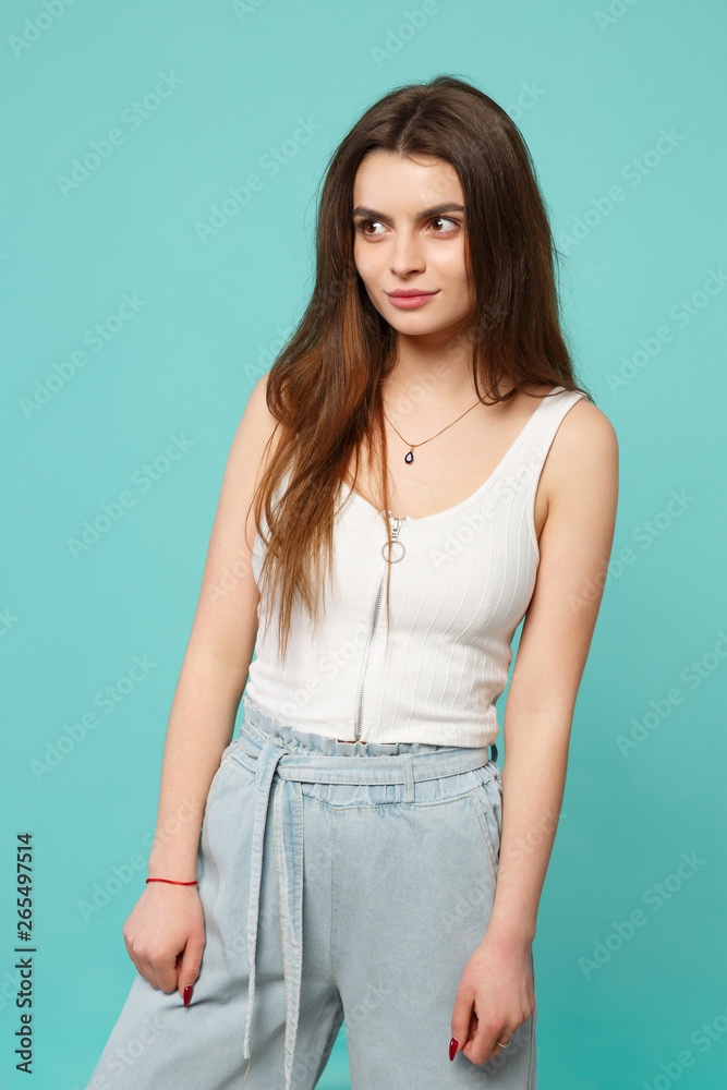 Portrait of smiling attractive young woman in light casual clothes looking aside isolated on blue turquoise wall background in studio. People sincere emotions, lifestyle concept. Mock up copy space. Portrait of smiling attractive young woman in light casual clothes looking aside isolated on blue turquoise wall background in studio. People sincere emotions, lifestyle concept. Mock up copy space.