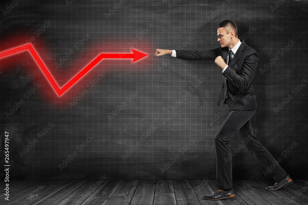 Businessman hitting red diagram arrow on black background Businessman hitting red diagram arrow on black background