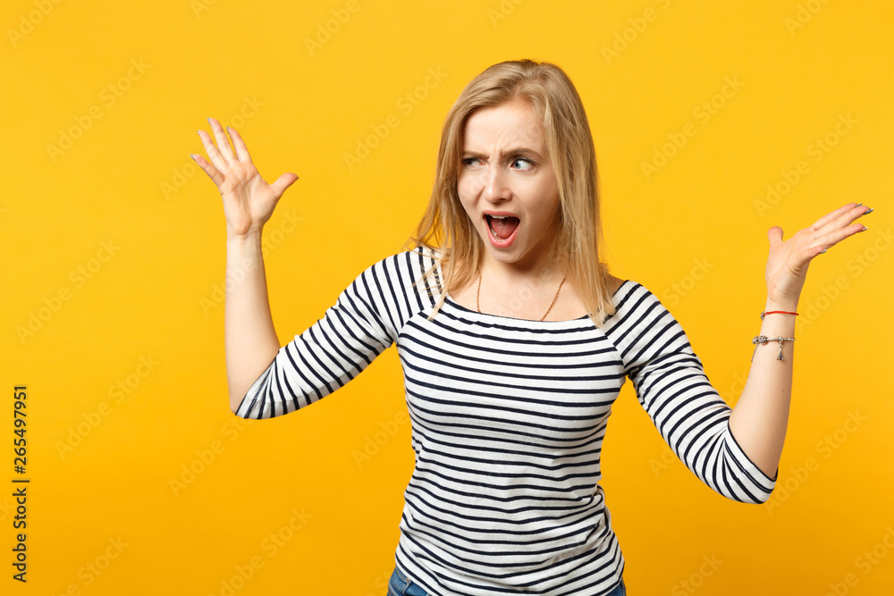 Irritated perplexed young woman in striped clothes looking aside, spreading hands, screaming isolated on yellow orange wall background. People sincere emotions, lifestyle concept. Mock up copy space. Irritated perplexed young woman in striped clothes looking aside, spreading hands, screaming isolated on yellow orange wall background. People sincere emotions, lifestyle concept. Mock up copy space.