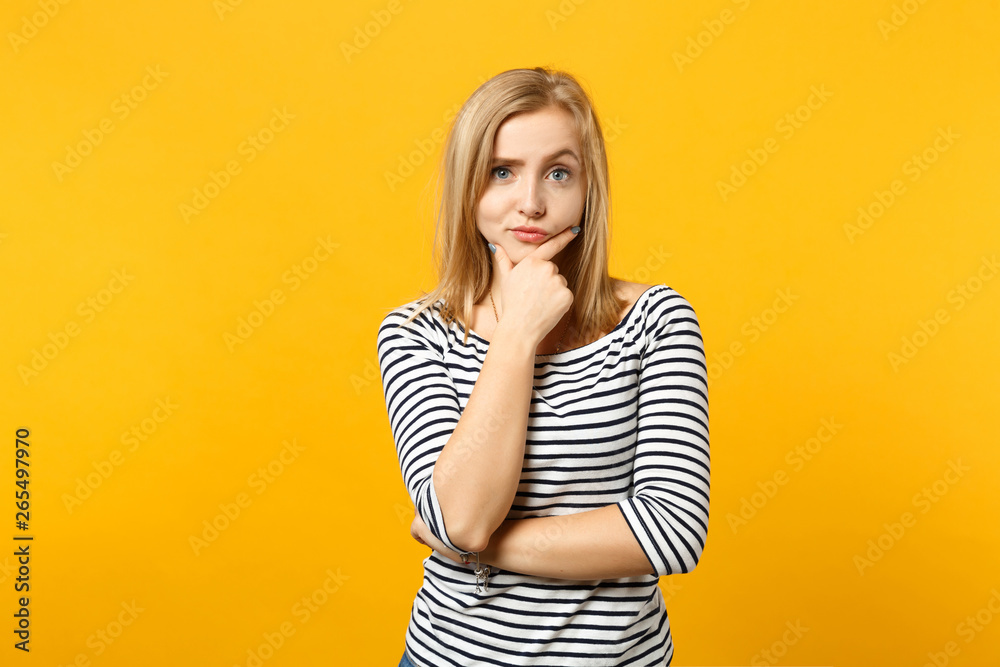 Portrait of puzzled young woman in striped clothes looking camera, put hand prop up on chin isolated on yellow orange wall background. People sincere emotions, lifestyle concept. Mock up copy space. Portrait of puzzled young woman in striped clothes looking camera, put hand prop up on chin isolated on yellow orange wall background. People sincere emotions, lifestyle concept. Mock up copy space.