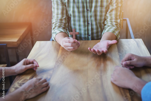 фотографія Close up of Young christian man holding small wooden cross in hands while explains about Jesus story and sharing gospel to his unbeliever friends around wood table indoor ,  great commission concept