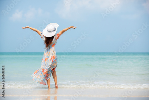 Relax traveler woman in dress with sun hat hands up standing on beach enjoys her tropical vacation , lifestyle travel summer concept