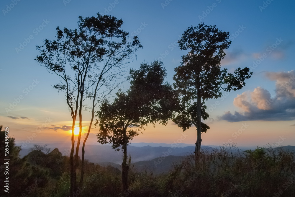 Mountain view evening silhouette of the trees with colorful of yellow sun light with blue sky background, sunset at Phu Langka Forest Park, Phayao, northern of Thailand.