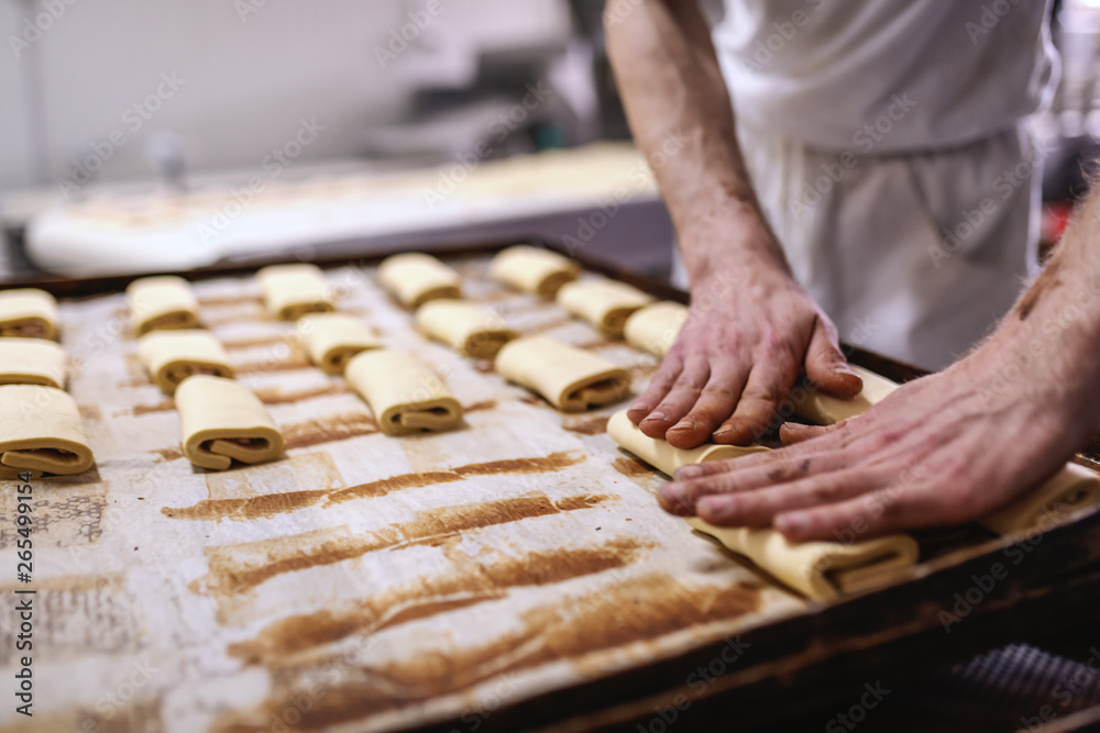 Caucasian baker in white uniform putting pastry on baking tray. Bakery interior.