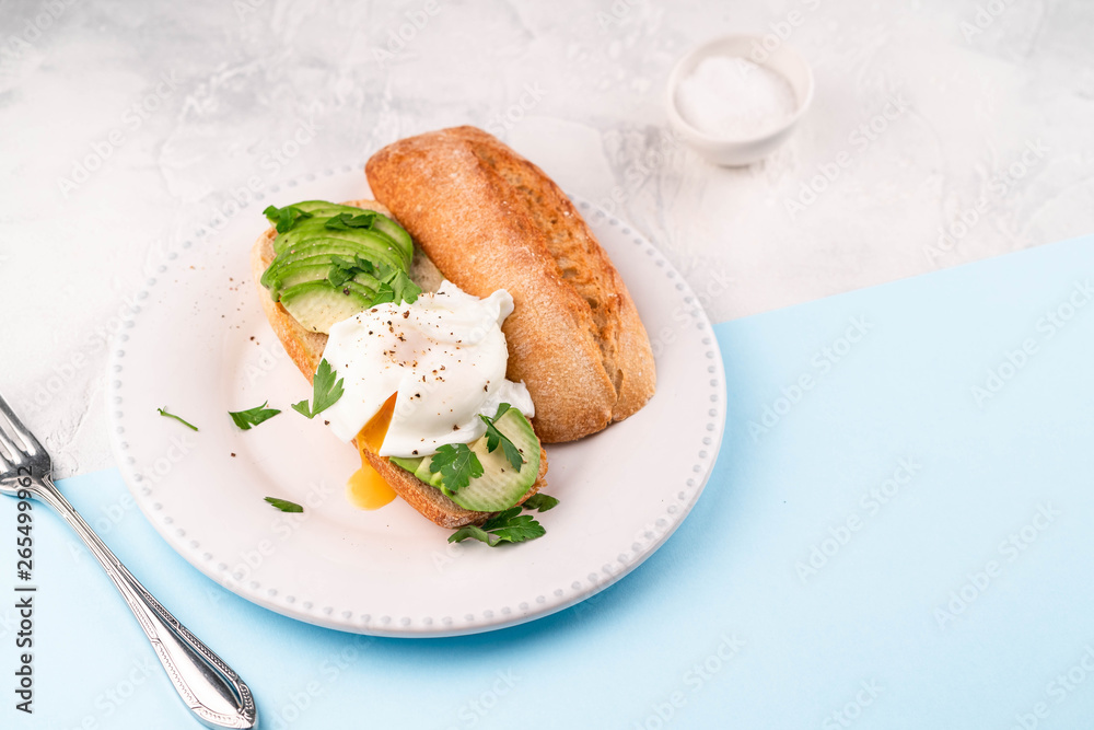 poached egg and avocado on bread on white plate, on blue paper and white backdrop poached egg and avocado on bread on white plate, on blue paper and white backdrop