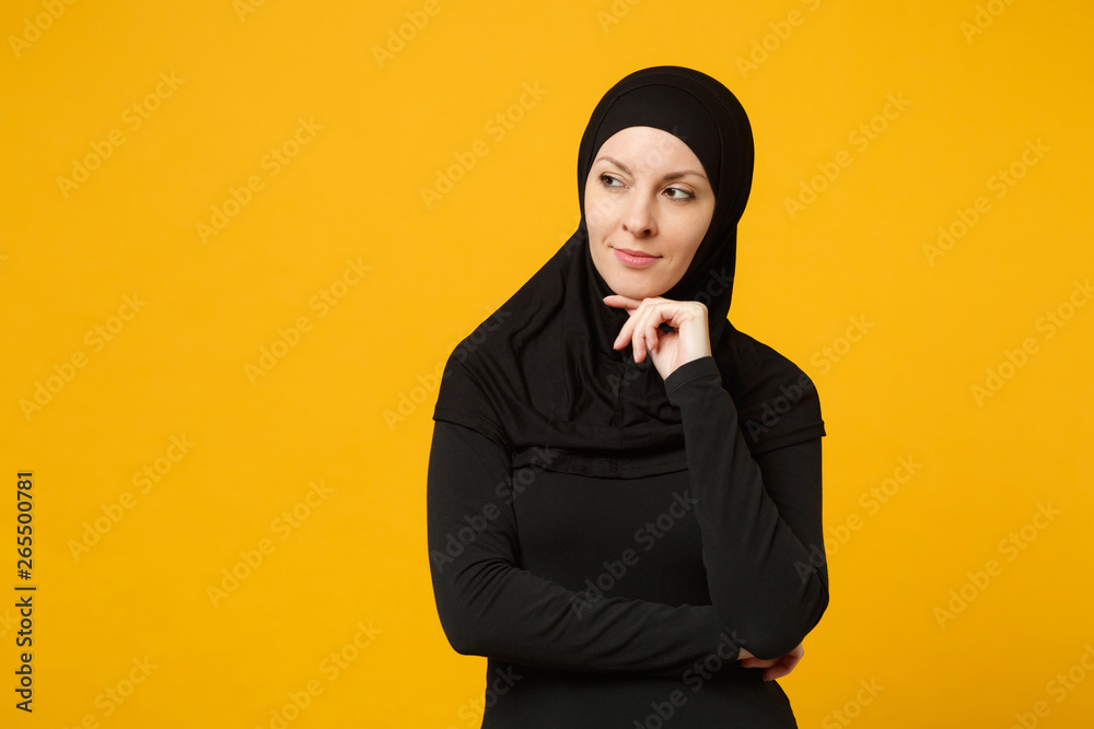 Smiling beautiful young arabian muslim woman in hijab black clothes looking aside camera isolated on yellow wall background, studio portrait. People religious lifestyle concept. Mock up copy space. Smiling beautiful young arabian muslim woman in hijab black clothes looking aside camera isolated on yellow wall background, studio portrait. People religious lifestyle concept. Mock up copy space.