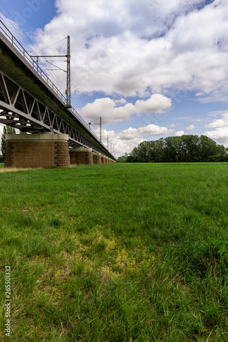 Meadow with a train bridge leading into far view. Clouds over the vertical scenery.