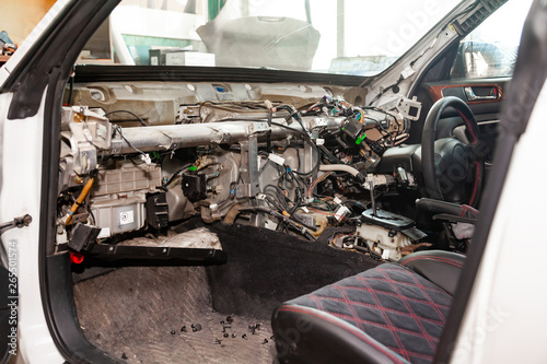 A large tangle of ravel multicolored wires from the car wiring lies in the cabin of dismantled car with connectors and plugs, a view through the window inside the battered car. Auto service industry