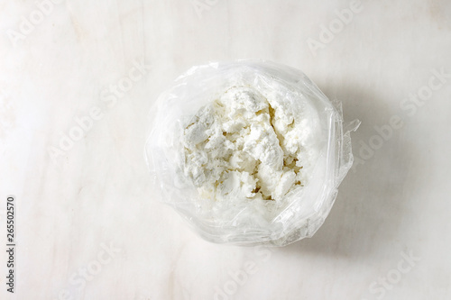 Fresh organic cottage cheese in opened plastic bag over white marble background. Flat lay, copy space