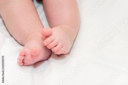 Feet newborn baby on a white bedspread. Small baby legs close up.