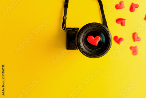 Flat lay of mirorless camera with lens and love red hearts on yellow background, engagement or couple wedding