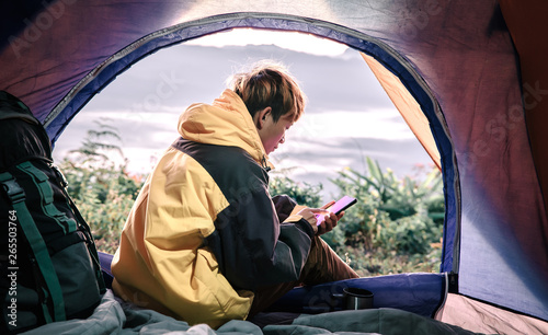 Young male hiker using mobile phone inside a tent in morning enjoying the leisure and freedom.