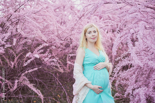 Spring mood, beautiful pregnant woman smell flowering tree, enjoying nature, pink floral garden. future mother relaxing and enjoying life in nature
