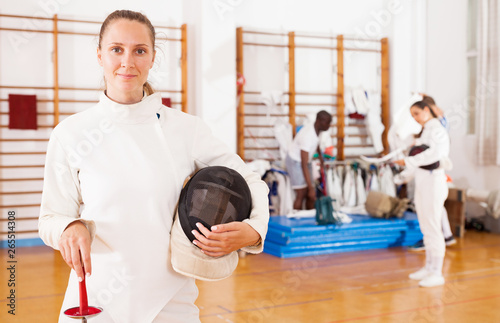 Sporty young woman in uniform standing at fencing workout