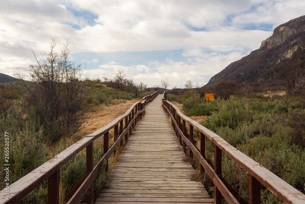 Wooden walkway in Lapataia bay, Tierra del Fuego national park, in a winter cloudy day, surrounded by nature and mountains in autumn colors