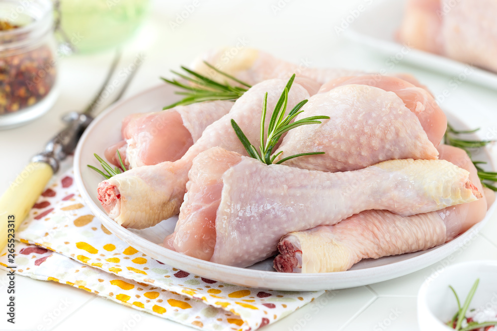 Fresh raw chicken drumsticks on a plate with sprigs of rosemary ready to be cooked Fresh raw chicken drumsticks on a plate with sprigs of rosemary ready to be cooked
