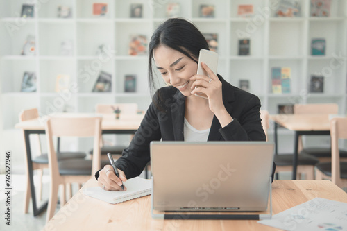 Professional working woman talking with mobile phone and writng document for listing information data.Working in office with technology concept. photo