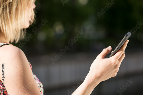 a young woman holding a black smartphone in her right hand such that the screen is not visible