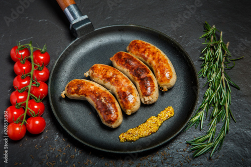 top view round pan with four fried sausages and granular mustard