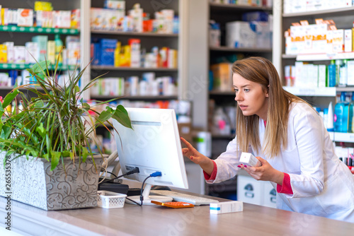 Pharmacist making prescription record through computer in pharmacy. Portrait of female pharmacist working with computer behind counter in pharmacy
