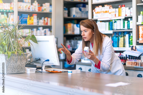 Portrait of pharmacist standing at counter in pharmacy. Pharmacist using the computer at the pharmacy. Medicine, healthcare and technology concept