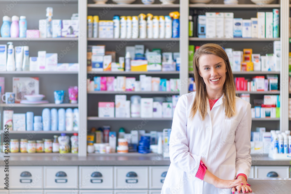 Medicine, pharmaceutics, healthcare and people concept. Portrait of a happy female pharmacist. Cheerful pharmacist chemist woman standing in pharmacy drugstore