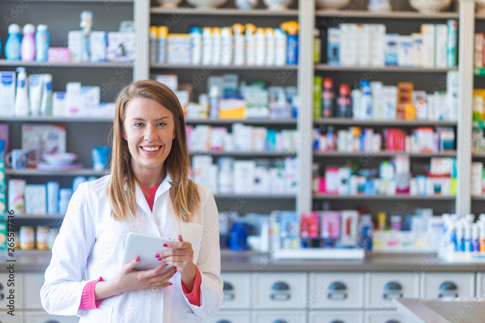 Smiling pharmacist chemist woman standing in pharmacy drugstore, looking at camera. Medicine, pharmacy, people, health care and pharmacology concept - happy young woman pharmacist over drugstore