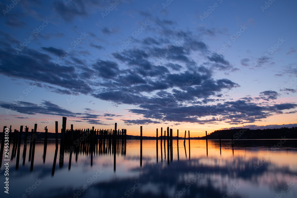 long exposure of dramatic sunset over water with pilings and reflection