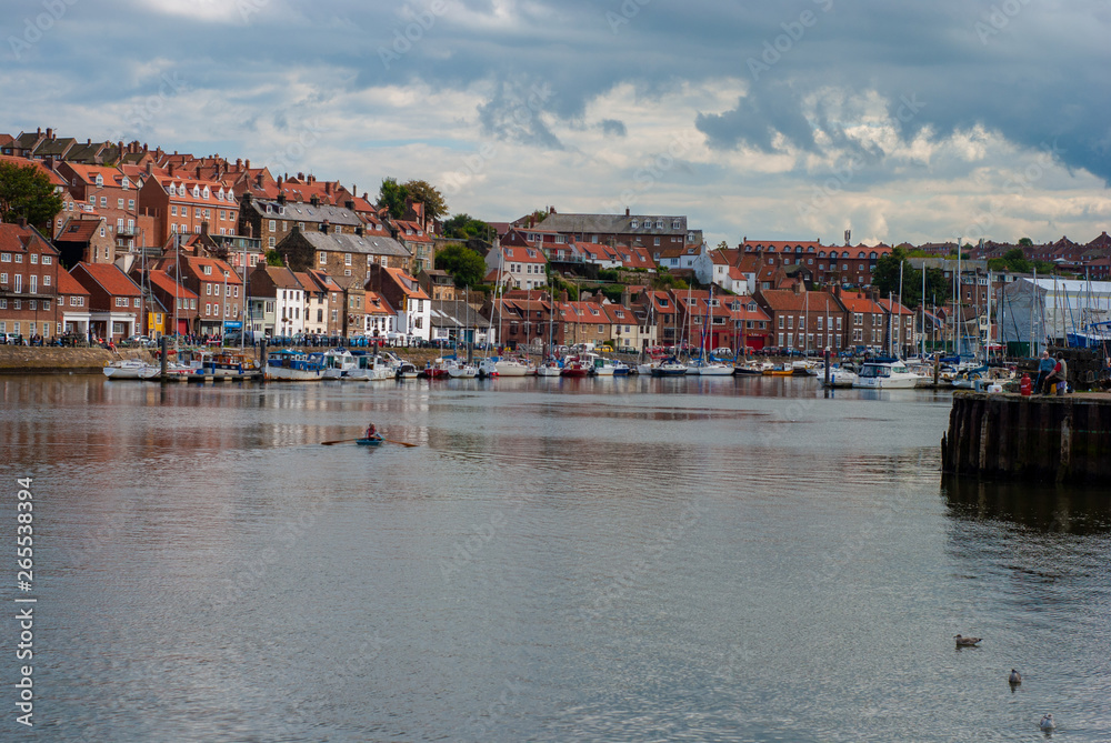 Whitby Harbour on a hot summers day with dark clouds and an islotaed rowing boat on the water.