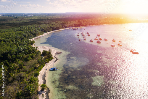 Aerial view from drone on caribbean beach with palm trees and speed boats floating in Atlantic ocean  sunset time