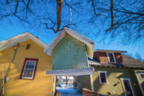 Closeup of a bird house between two real houses - blue skies and overhanging tree - city neighborhood