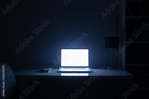 Room illuminated by a computer screen at night, no people. Empty workplace lit by a laptop display in the darkness, late work, overtime concept photo