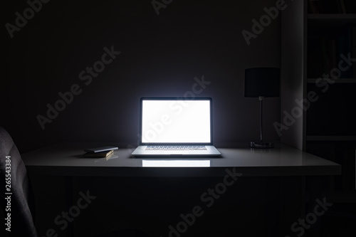 Room illuminated by a computer screen at night, no people. Empty workplace lit by a laptop display in the darkness, late work, overtime concept photo