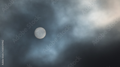 Sun filtered by dark clouds in the sky - looks like the moon but you can see sun spots - blue skies visible - as seen from Minnesota on January 11, 2014