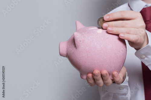 Children's hands put a coin in a pink piggy bank. Business concept. Close-up