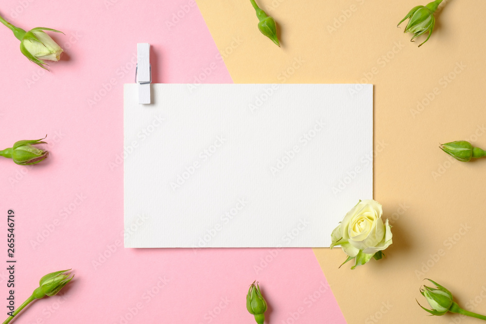 Blank white paper with clothespin and flowers on pink and yellow background. Top view, tender minimal flat lay style composition. Women desk, fashion blogger, love, tenderness concept.