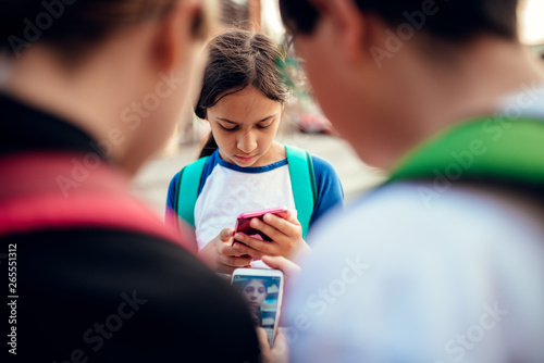 Worried girl standing between friends and using smart phone photo