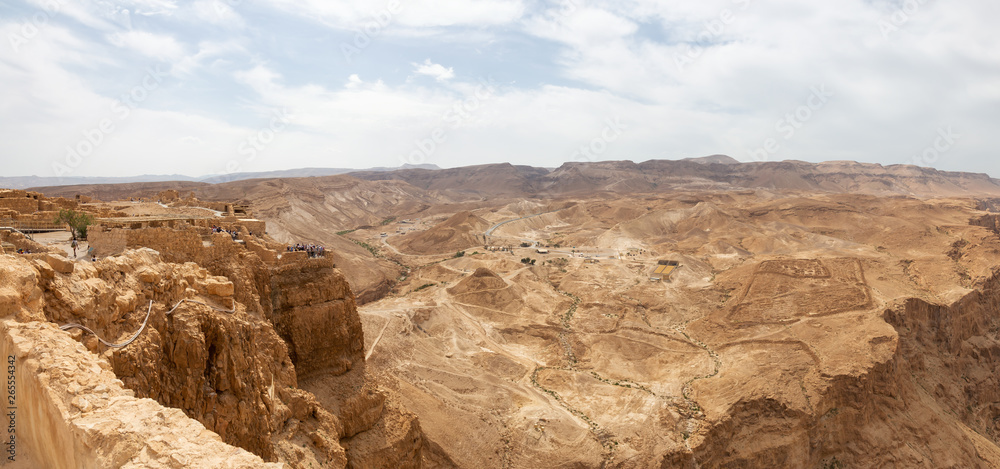 Beautiful panoramic view of an ancient fortress on top of a mountain during a cloudy and sunny day. Taken in Masada National Park, Israel.