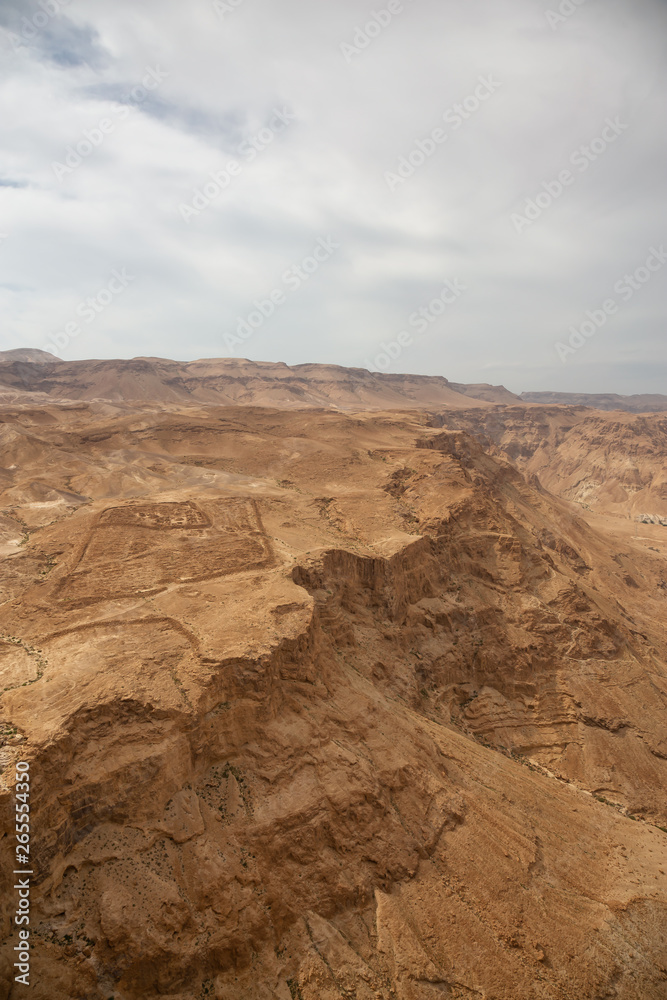 Beautiful aerial view of a mountain desert landscape during a cloudy and sunny day. Taken in Masada National Park, Israel.