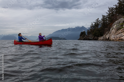 Couple adventurous female friends on a red canoe are paddling in the Howe Sound during a cloudy sunset. Taken in Horseshoe Bay, West Vancouver, BC, Canada. © edb3_16