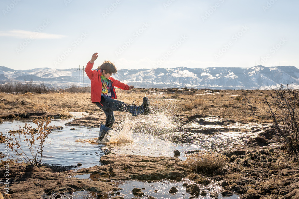 Young boy in red jacket kicking water in mountains on a hike