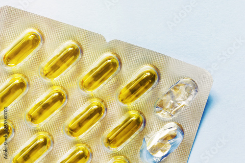 Oil-filled softgel capsules in blister pack, two capsules missing on pastel blue background . Healthcare, vitamins, supplements daily intake concept. Fish oil, omega3, vitamin D, vitamin E deficiency.