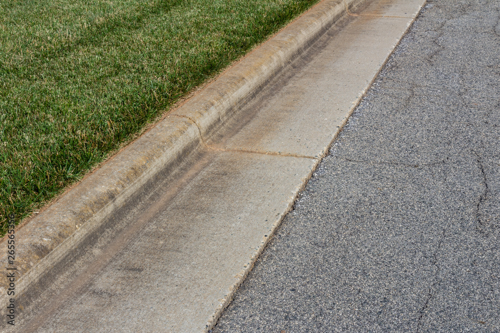 Angled view formed concrete curb, green grass and asphalt street, horizontal aspect
